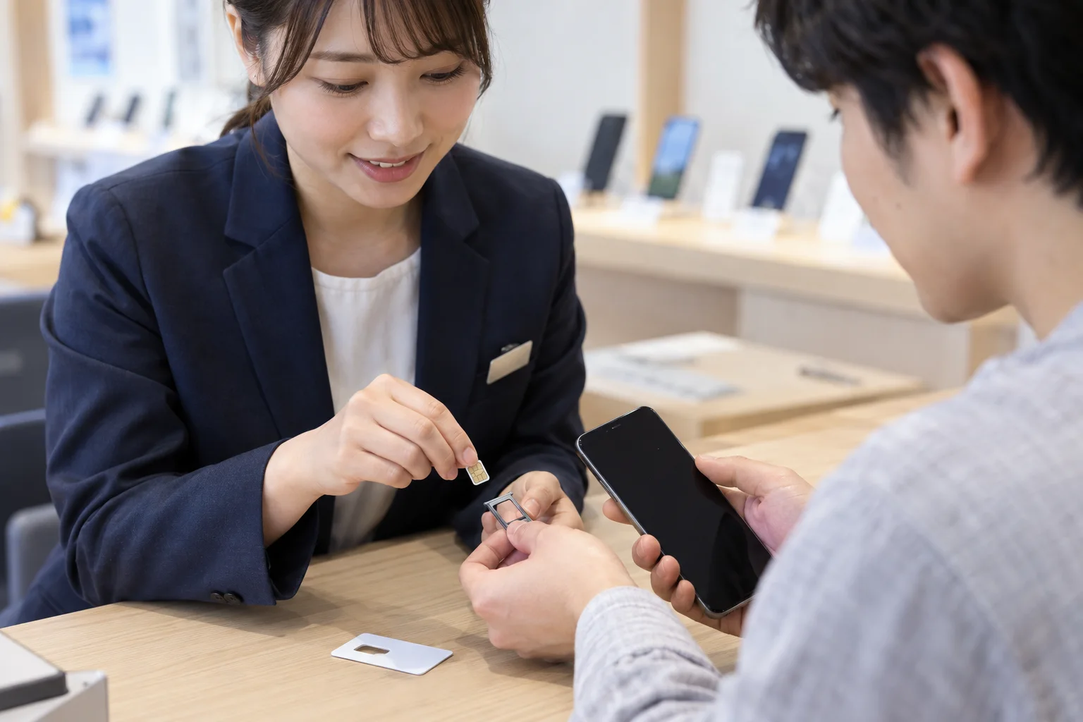 A phone shop employee helps a customer with a smartphone SIM tray and SIM card.